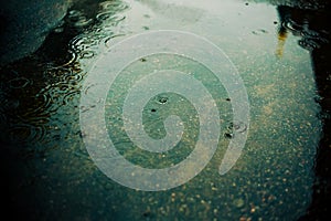 Raindrops fall on the water surface of a puddle on the street in the city and create circles. Cloudy weather in the city