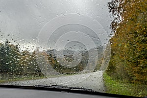 Raindrops on the glass on the background of a bright autumn road