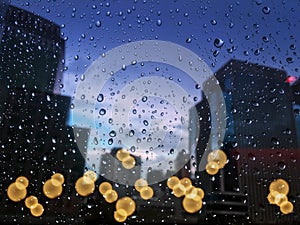 Raindrops on glass with cityscape in the background blurred and the background city bokeh light. City life in the rainy season eve