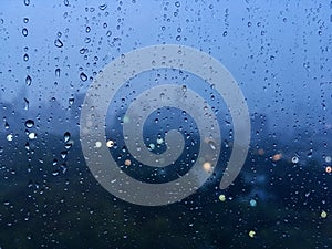 Raindrops on glass with cityscape in the background blurred and the background city bokeh light. City life in the rainy season eve