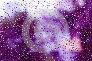 Raindrops on glass with a purple tint.