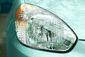 Raindrops on a headlight of metallic blue car close-up