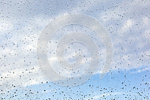 Raindrops on misted window glass against a blue sky