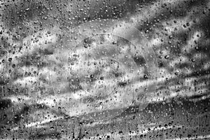 Raindrops on misted window glass against a blue sky. Black and white image