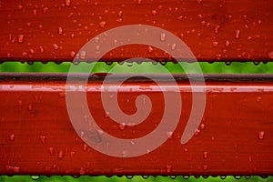 Raindrops on a painted red wooden structure. after the rain. Red bench element