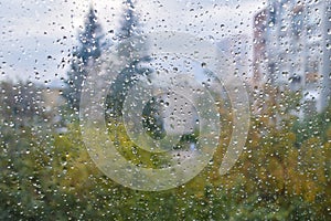 Raindrops on a rainy day on the window pane. Autumn cloudy weather through glass covered with rain drops.