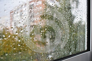 Raindrops on a rainy day on the window pane. Autumn cloudy weather through glass covered with rain drops.