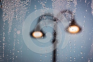 Raindrops running on window glass lit by street lamps. Blurred abstract background