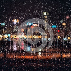 Raindrops streak down a window, softening a distant city skyline filled with colorful, photo