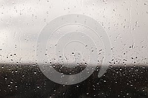 Raindrops on window background. Water droplets on glass surface. Rainy weather. Rain drops on background of gray clouds. Rainy day