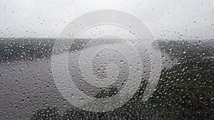 Raindrops on the window close up. rainy weather. river flowing on the background