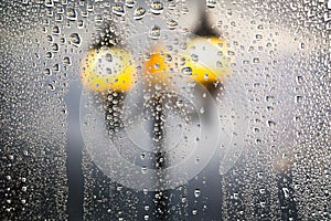 Raindrops running on window glass. Beautiful street lamps on the rain. Blurred abstract background