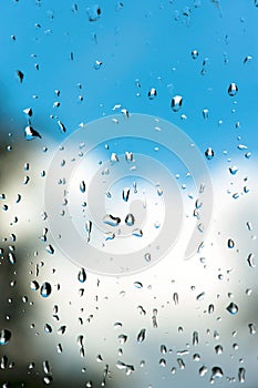 Raindrops on window glass with bright blue cloudy sky backgroun