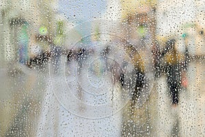 Raindrops on window glass, people walk on road in rainy day, blurred motion abstract background. Concept of shopping