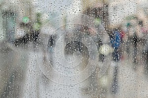 Raindrops on window glass, people walk on road in rainy day, blurred motion abstract background. Concept of shopping