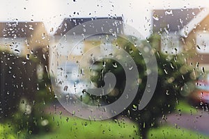Raindrops on window glass in rainy day with blurry tree and house background, View looking trough window with water drops texture
