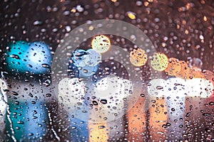 Raindrops on the windshield of a car at night and blurry spots of light