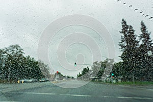 Raindrops on the windshield on a rainy day, traffic light background, California