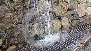 Rainfall wada falls in a stream on a sewer grate near a wall of raw stone