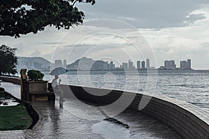 Raining in Park that near the Coast with a Man Holding Umbrella and Seeing Seascape and Cityscape of George Town, Penang, Malaysia