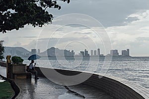 Raining in Park that near the Coast with a Man Holding Umbrella and Seeing Seascape and Cityscape of George Town, Penang, Malaysia