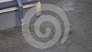 Rainwater flows down from the roof of the building through a drainpipe. Downpipe and splashes from the rain close-up. Heavy rain