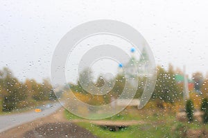 Rainy autumn day, view of the autumn forest and the church through the wet window. Autumnal sad landscape