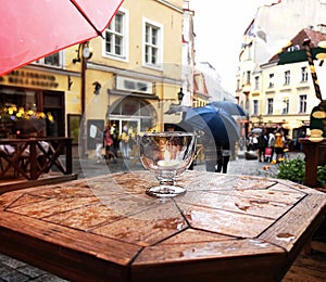 Rainy city people walk with umbrellas on wooden table glass with candlr light rain drops in medieval street houses in Tallinn old