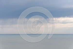 Rainy clouds over a calm sea, strip of rain on horizon, soft focus