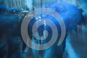 Rainy cold evening in the city. Silhouettes of people under umbrellas. Abstract blurred background in blue tones.