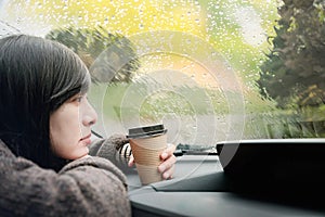 Rainy Day or Bad Weather in a Vacation Concept. a Sadness Woman with Hot Coffee sitting in Car and Looking Outside through Window