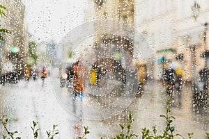 Rainy day in city. People seen through raindrops on glass. Selective focus on the raindrops