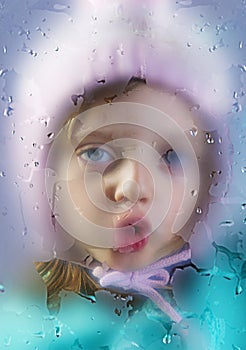 Rainy day - face of a little girl behind a dewy window