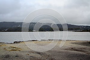 Rainy day at lake Rotorua. Sandy beach leading to grey water and clouds low over distant mountains