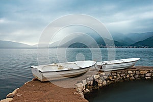 Rainy day. Two white fishing boats on the shore. Montenegro, Bay of Kotor