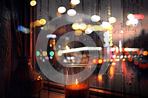 Rainy evening city view,car traffic light, from window people walk  , candle light reflection rain drops on glass urban