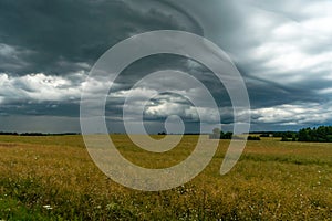 A rainy gray cloud hovered over the field. A hurricane over an agricultural field. Dirt country road, dramatic scene