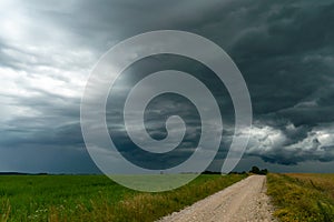 A rainy gray cloud hovered over the field. A hurricane over an agricultural field. Dirt country road, dramatic scene