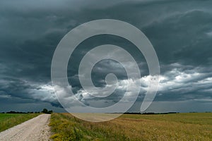 A rainy gray cloud hovered over the field. A hurricane over an agricultural field. Dirt country road, dramatic scene