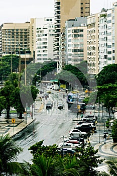 Rainy intersection showing cars and tour buses surrounded by trees apartments, and hotels
