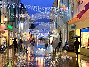 Rainy  weather in the City, Christmas street at night  ,people walking with umbrellas , rain drops reflection on windows vitrines