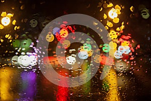 Rainy weather, night city, raindrops through the glass, abstract background from the light of cars and traffic lights, defocus,