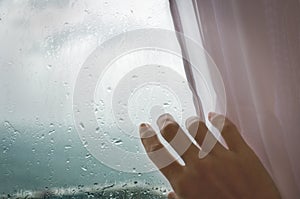 Rainy weather - a woman`s hand pulls the blind from the rainy window.