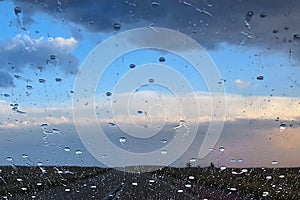 Rainy windshield glass photo. Cloudy weather road view through rain drops on car window. Inside vehicle. Road trip