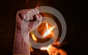 Raised clenched fist with burning flames from bonfire in background. Stock photo with socialism, communism, revolution, workman an