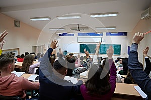 Raised hands and arms of large group of people in class room