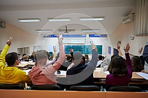 Raised hands and arms of large group of people in class room