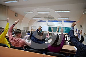 Raised hands and arms of large group of people in class room