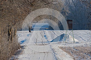 Raised hunting hide near country road near field in winter with snow and rime on trees