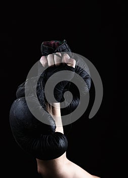 Raised up man`s hand holds a pair of old black leather boxing gloves